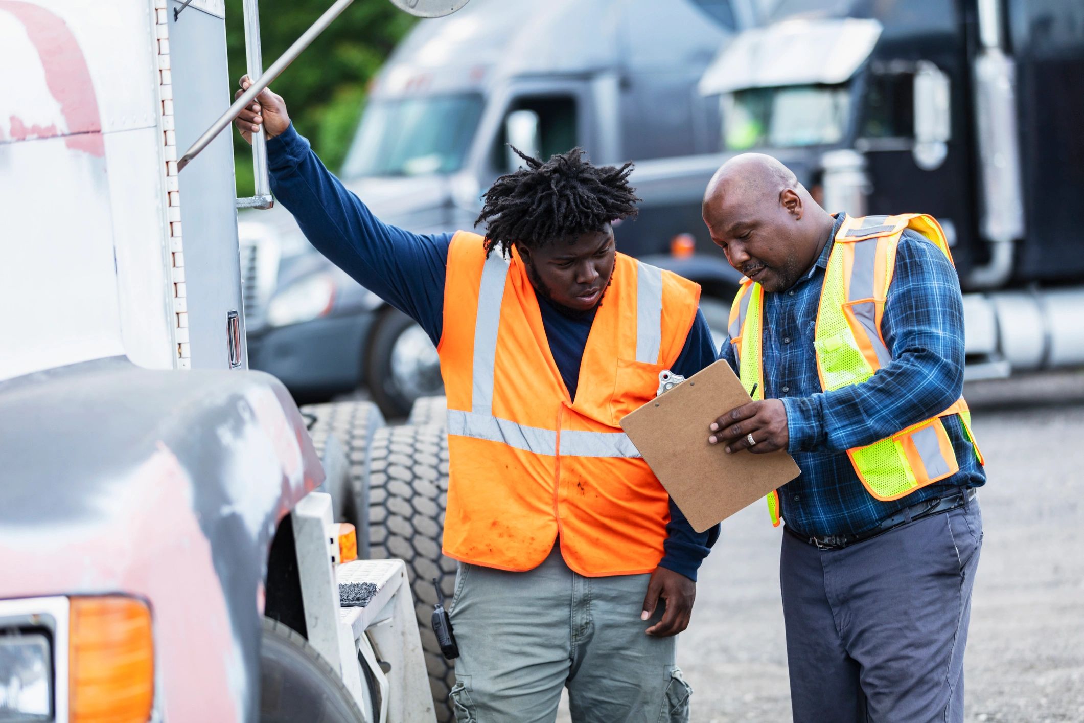 Two people reviewing a clipboard beside a semi-truck